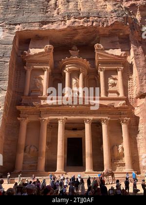 Tourists amass outside Al-Khazneh, 'The Treasury', aka Khazneh el-Far'oun (treasury of the pharaoh), is one of the most elaborate rock-cut tombs in Petra, a city of the Nabatean Kingdom inhabited by the Arabs in ancient times. As with most of the other buildings in this ancient town, including the Monastery (Arabic: Ad Deir), this structure was carved out of a sandstone rock face.It is thought that Al-Khazneh was built as a mausoleum and crypt at the beginning of the 1st century AD during the reign of Aretas IV Philopatris. Petra, Jordan Stock Photo