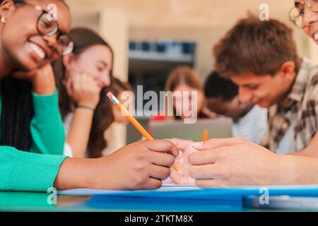 Close up and cropped portrait of a hand writing on a note book focus on a pencil. Unrecognizable female teenage student learning on a university library desk with her classmates. Note pad and pen. High quality photo Stock Photo