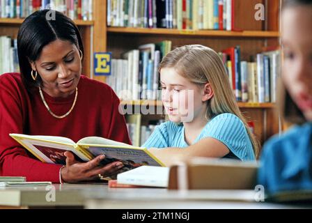 An African-American school librarian helping a call Caucasian middle school student to read a Science book Stock Photo