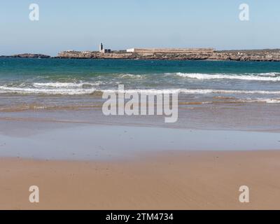 Waves rolling onto a sandy beach with an island behind in the city of Essaouira "The Windy City", Morocco. December 20, 2023 Stock Photo