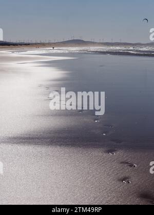 Footprints on a sandy beach with wind turbines, surfer and kite behind in  Essaouira 'The Windy City', Morocco. December 20, 2023 Stock Photo