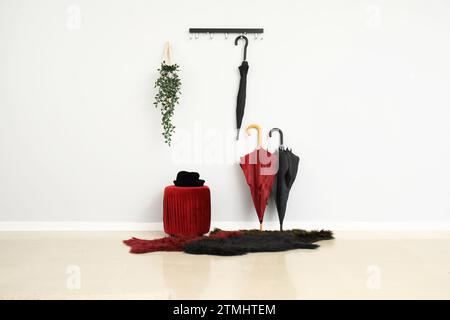 Hat on stylish pouf and umbrellas near light wall Stock Photo