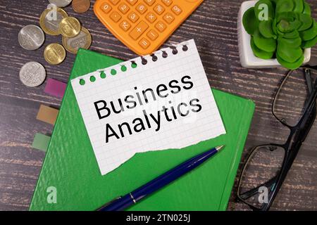 business analytics, text concept. Office workplace table with calculator, graphs, reports and the text business analytics on a small piece of paper on Stock Photo