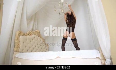 Sexy young woman in lingerie dancing erotic dance on bed
