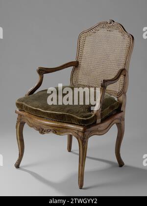 Arm chair with wicker seat and back and with a loose pillow. OVERHOUT S-shaped legs and scalloped bottom line., Anonymous, 1740 Arm chair of walnut with a thatched seat and back. Decorations have been applied to the swellings of the S-shaped legs and on the scalloped bottom line at the front. The S-shaped armrest fabrics make outwards and support the stretched S-shaped armrests. The styles and sills of the back window are sculpted; The upper sill carries an ornament in the middle. France wood (plant material). walnut (hardwood). Arm chair of walnut with a thatched seat and back. Decorations ha Stock Photo