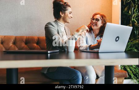 Female colleagues having a discussion while working on a laptop, developing software and utilizing cutting-edge technology. With happy faces, they exe Stock Photo