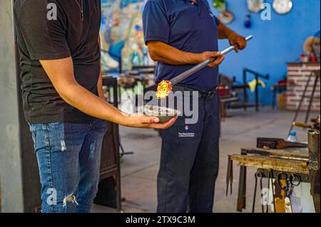 Two men demonstrate how to dip hot glass into colorful beads in a workshop in Baja California, Mexico. Stock Photo