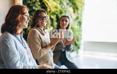 Multitasking business professionals applaud and celebrate a successful meeting. The office environment is filled with teamwork and collaboration as co Stock Photo