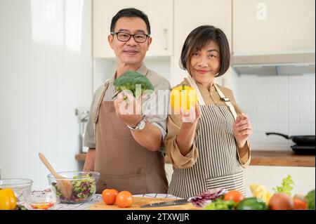 Lovely Asian couple are in the kitchen, cooking together, posing with fresh vegetables. Home cooking, domestic life, adult couple Stock Photo