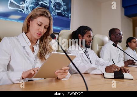 Female doctor using tablet pc while sitting at conference with her colleagues Stock Photo