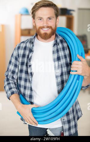 builder carrying a reel of blue pipe across his body Stock Photo