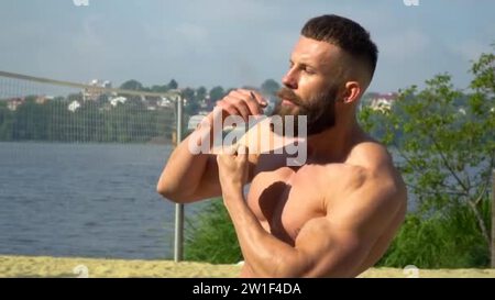Bodybuilder smokes a cigarette. Young bearded athletic bodybuilder plays  sports outdoors