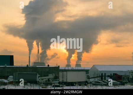 The smoke from the CHP chimneys blocked the sun in the evening sky at sunset. In the foreground is a parking lot with a white truck on it. Stock Photo