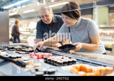 Couple chooses sushi near refrigerator in supermarket Stock Photo