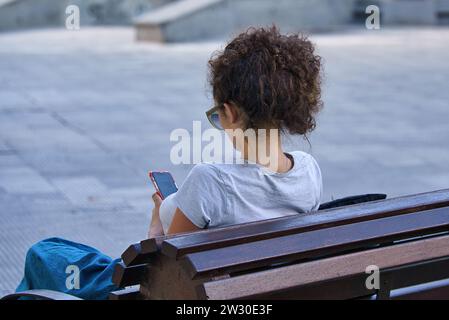 Solitude in the Digital Age: A young lady finds her own space in the park, immersed in the virtual world on her phone Stock Photo