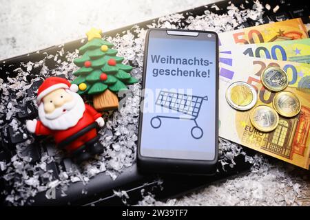FOTOMONTAGE, Smartphone mit Aufschrift Weihnachtsgeschenke und Einkauswagen, Geldscheine, Weihnachtsmannfigur und Tannenbaum auf Computertastatur Stock Photo