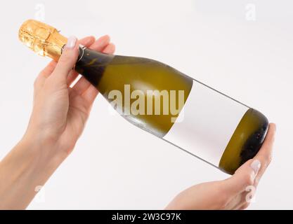 Image of a bottle of champagne in female hands. Light studio background. Mixed media Stock Photo
