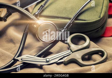 Stethoscope lies on a military uniform with scissors and a first-aid kit. The concept of health care, military insurance, state care. Top view. Mixed Stock Photo