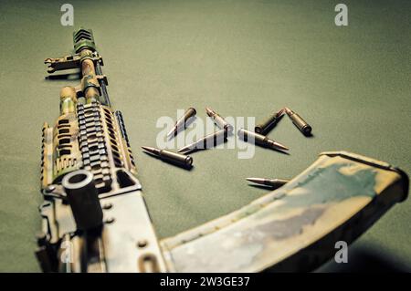 On a green background lies a camouflage machine gun along with bullets. View from above. The concept of war, political conflict. Mixed media Stock Photo