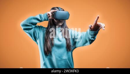 Image of a woman in virtual reality glasses on an orange background. Cyber space. Future technologies concept. Mixed media Stock Photo