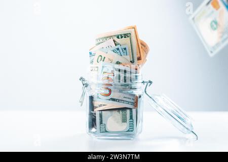 Glass piggy bank full of money. Banknotes are strewed from above. The concept of squandering. Mixed media Stock Photo