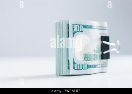 Pack of hundred-dollar bills lies on a white table fastened with a paperclip. The concept of savings during the crisis. Mixed media Stock Photo