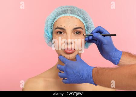 Doctor with pencil preparing patient for cosmetic surgery operation on pink background Stock Photo