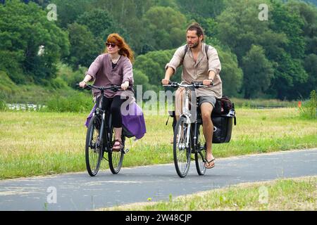 A young couple cycling together with loaded panniers on a river path during a summer bike touring adventure in Europe Stock Photo