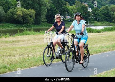Two senior women ride a bicycle on a cycle path along the river Elbe Saxony Germany Stock Photo