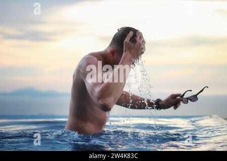 Young man in the infinity pool on a background of beautiful sunset. Tourism and vacation concept. Stock Photo