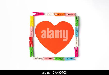 Red heart inside square made with multicolored wooden clothespins on white background. Stock Photo
