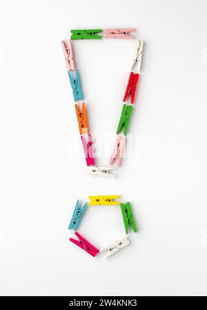 Exclamation mark laid out of colored wooden clothespins on white background. Top view. Stock Photo