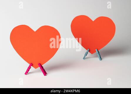 Two red paper hearts stands on wooden colored clothespins on white background. Minimal love concept. Space for text. Stock Photo