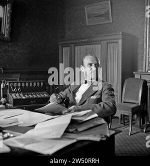 Gentleman with bow tie sitting behind desk with a small telephone switchboard to his right, presumably in the 1920s Stock Photo