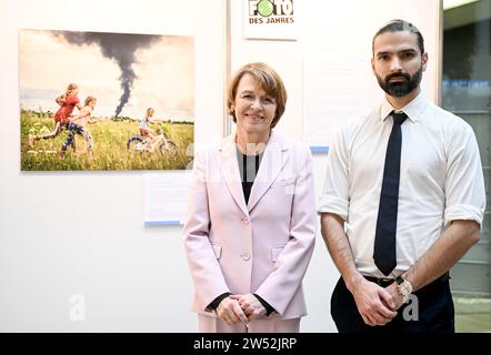 21 December 2023, Berlín: Elke Büdenbender, wife of German President Frank-Walter Steinmeier, poses with Polish photographer Patryk Jaracz in front of the winning image of the Unicef Germany Photo of the Year 2023 award, showing Ukrainian girls playing as a cloud of black smoke rises from an oil depot. Photo: Britta Pedersen/dpa Stock Photo