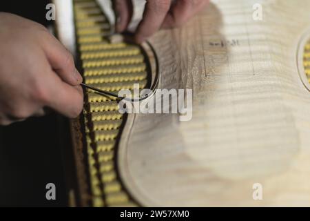 Unrecognizable luthier lute maker artisan hands in his workshop try, push and glue fillet purfling strips into carved inlaid wood channel, for a new Stock Photo