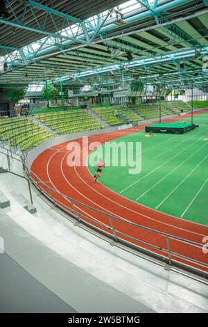 Person jogging in a stadium on a red running track, green pitch and yellow stands, covered area, Glaspalast, Sindelfingen, Germany Stock Photo