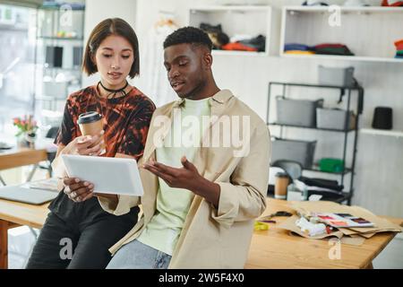 ambitious interracial designers with digital tablet and paper cup working on startup in print studio Stock Photo
