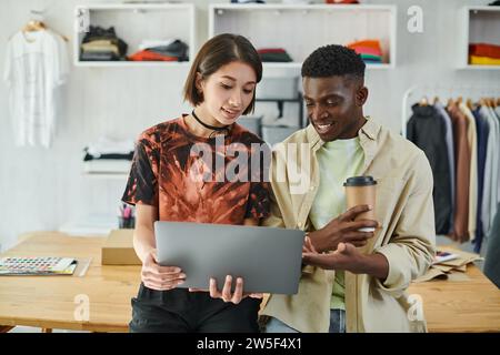 ambitious interracial designers looking at laptop while discussing startup in print studio, teamwork Stock Photo