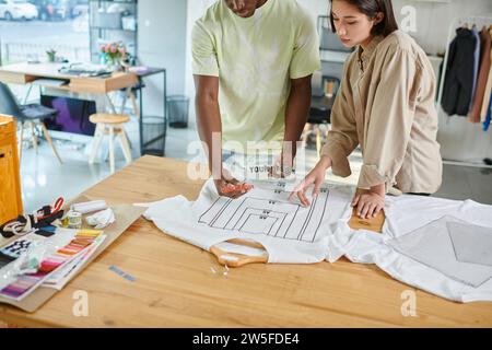 multiethnic designers working with text templates near t-shirt with format sizes in print studio Stock Photo