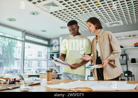 creative multicultural designers working with color palette near clothes in print studio, teamwork Stock Photo