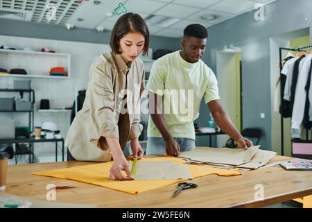 skilled interracial fashion designers measuring sewing patterns in print studio, small business Stock Photo