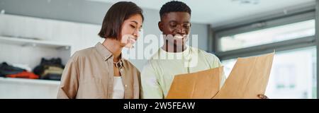 happy multiethnic fashion designers looking at sewing patterns in modern  print studio, banner Stock Photo