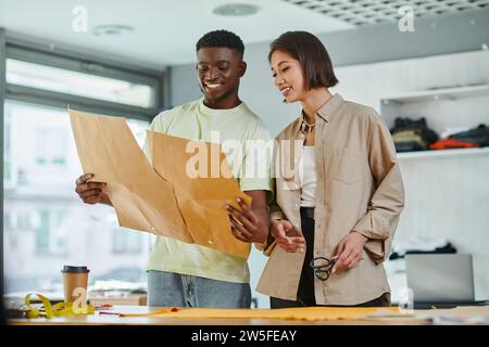 pleased multicultural clothes designers looking at sewing patterns in modern  print studio Stock Photo