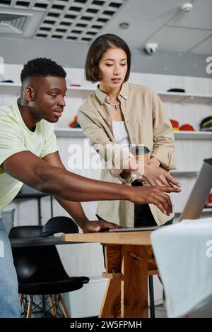 multiethnic designers pointing at laptop while working on new project in textile printing workshop Stock Photo