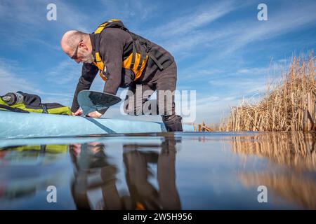 senior male paddler is boarding his stand up paddleboard for paddling workout on a lake Stock Photo