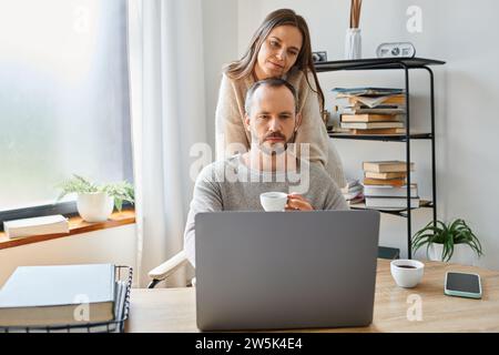caring woman supporting thoughtful husband sitting with coffee cup at laptop in home office Stock Photo