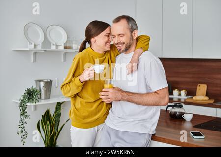 delighted child-free couple with coffee and fresh orange juice smiling with closed eyes in kitchen Stock Photo