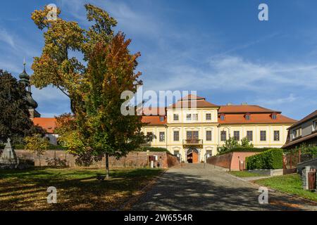 Svojsin, Czech Republic - October 13 2023: Front view of the newly renovated castle, a yellow building with red roof, cobblestone paving, a church Stock Photo