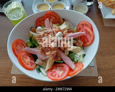 Fresh salad decorated with grilled chicken, ham, cheese, mushrooms and quail eggs on a deep white plate Stock Photo